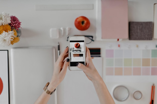 Photo of phone taking snapshot of office supplies on white background on table are stationery devices flowers and apple